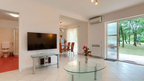 Una sala de estar moderna con un televisor de pantalla plana grande, una mesa de centro de vidrio y un comedor con sillas naranjas.