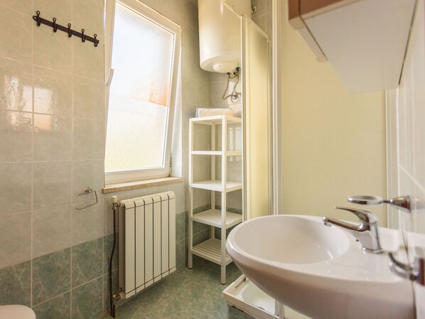 A bathroom with a white sink, a window with a curtain, a radiator, and a shelf unit.