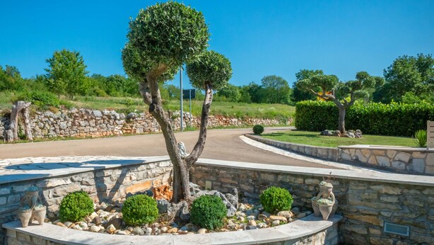 A landscaped area with a stone wall, a roundabout, and various shrubs and trees. - Vacation home Medica by Interhome (Pazin)