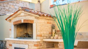A brick-built outdoor oven with a tiled roof, a vase with dried plants, and a table with a bowl of nuts. - Vacation home Medica by Interhome (Pazin)