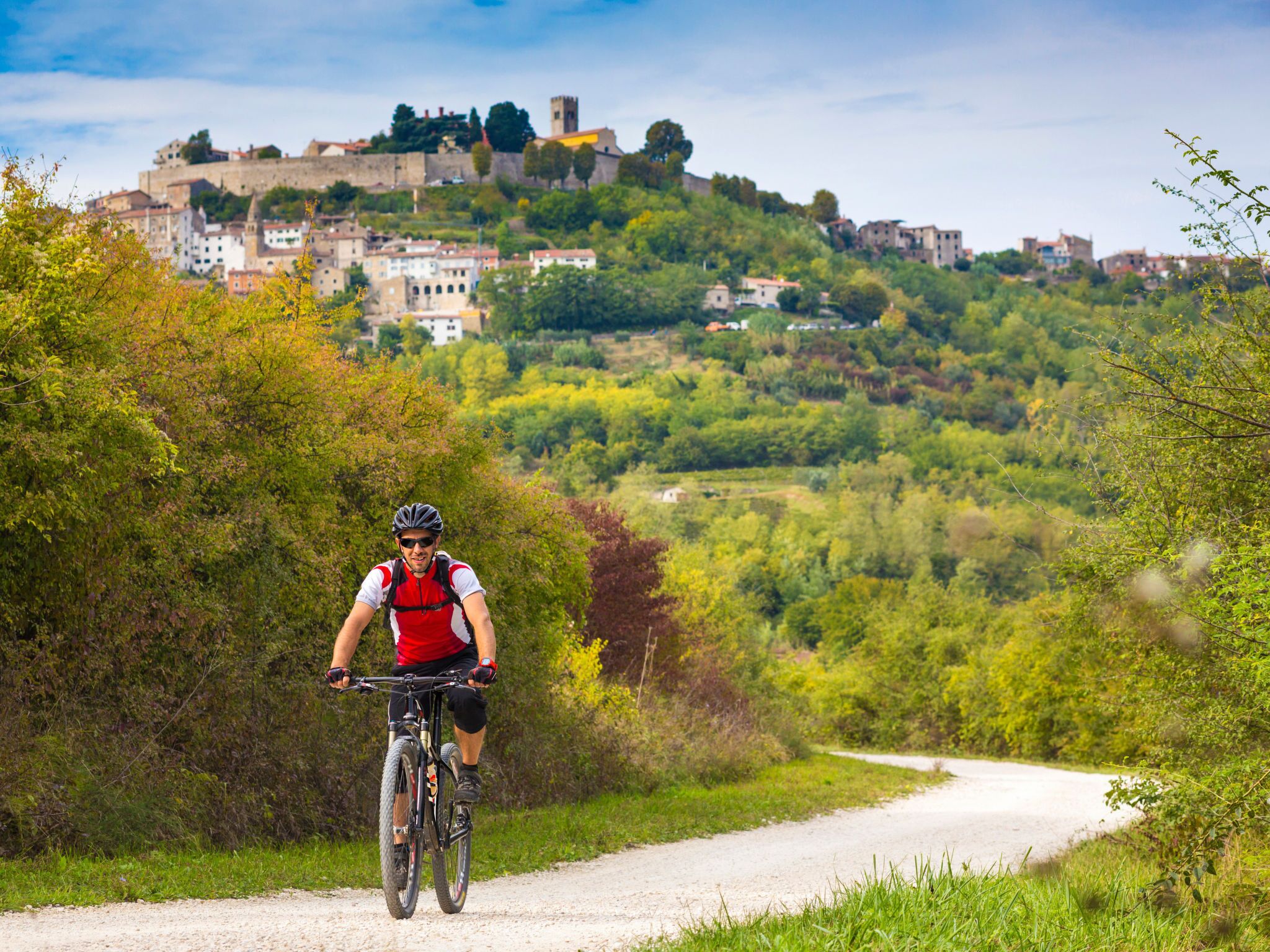 Un vététiste sur un sentier de terre, avec en arrière-plan une vue sur une ville historique perchée sur une colline.