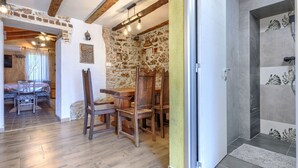 A rustic interior with exposed stone walls, wooden beams, and a dining area with a table and chairs.