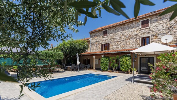 A stone building with a swimming pool, outdoor seating, and a covered area.