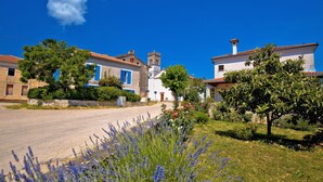A quaint village street with traditional buildings, a church tower, and lush greenery.