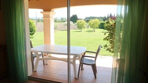 A patio with a table and chairs, a glass door, and a view of a green landscape. - Plan du Vas by Interhome (Valreas)