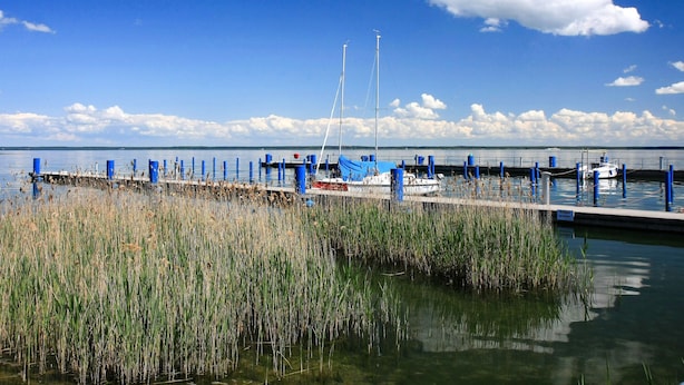 Marina com barcos atracados, um cais que se estende sobre a água e céu claro.
