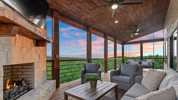 An outdoor deck with a fireplace, wicker furniture, and a view of the landscape. - Featured on Staycation: The Overlook | Pool, Pickleball, ATV Access & Views (Broken Bow)