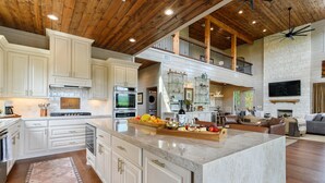 A spacious kitchen with white cabinets, a large island, and a dining area with a fireplace. - Featured on Staycation: The Overlook | Pool, Pickleball, ATV Access & Views (Broken Bow)