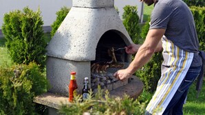 Henkilö grillaa lihaa ulkona kiviuunissa, ja lähellä on pullo ketsuppia ja pullo grillikastiketta.