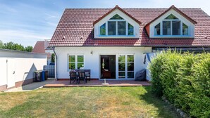 A two-story house with a red-tiled roof, a covered patio with a table and chairs, and a well-maintained lawn.