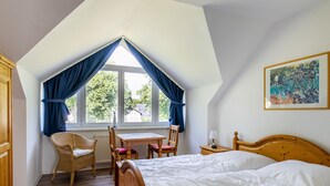 A bedroom with a sloped ceiling, a bed, a table with chairs, and a window with curtains.