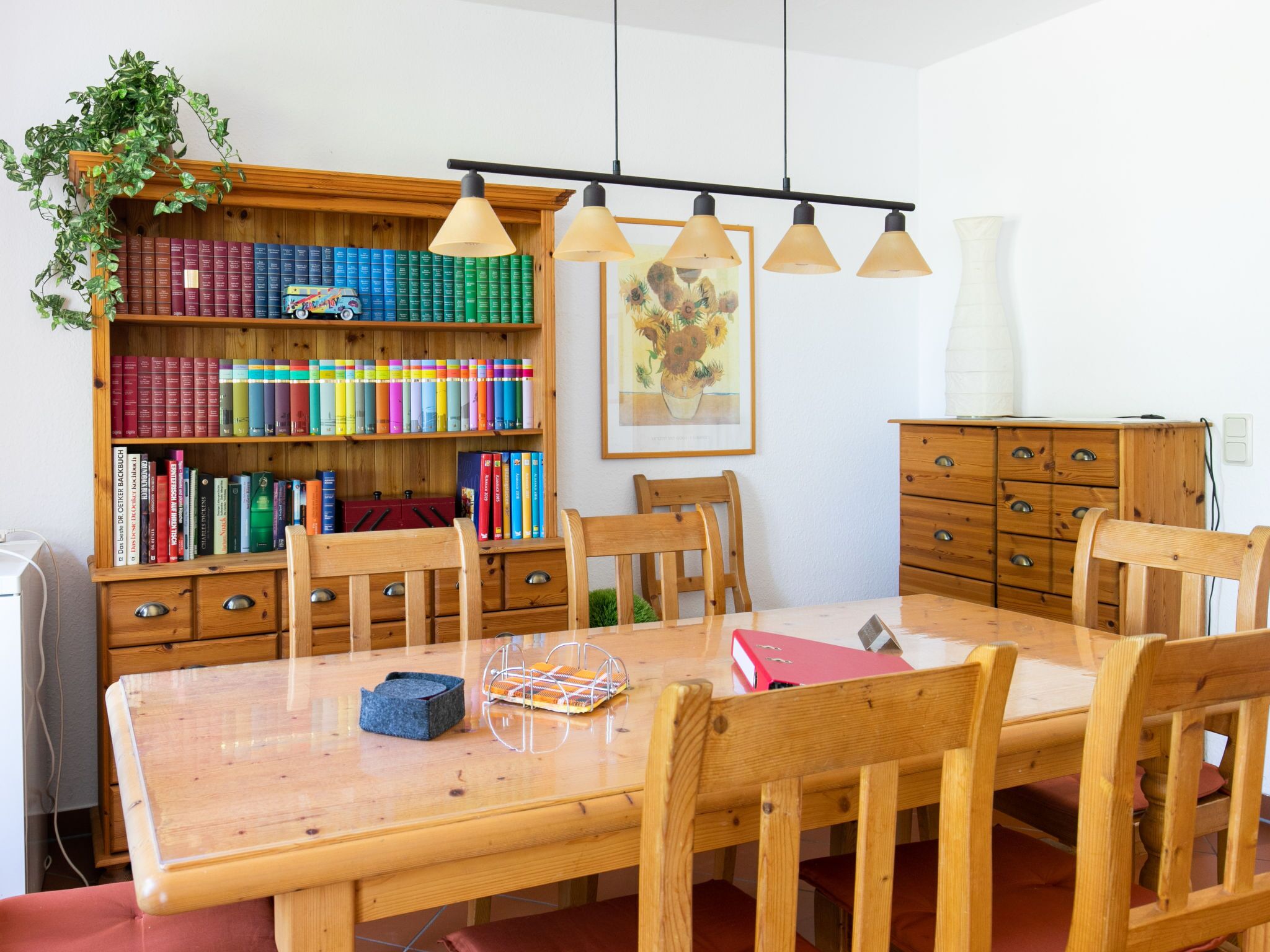 Een eetruimte met een houten tafel en stoelen, een boekenkast vol boeken en een schilderij aan de muur.