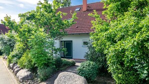 Ein Haus mit rotem Ziegeldach, umgeben von üppiger Vegetation und einem gepflasterten Weg.