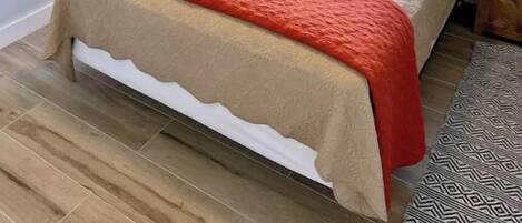 A neatly made bed with a red and beige bedspread, two pillows, and a small plant beside the window.