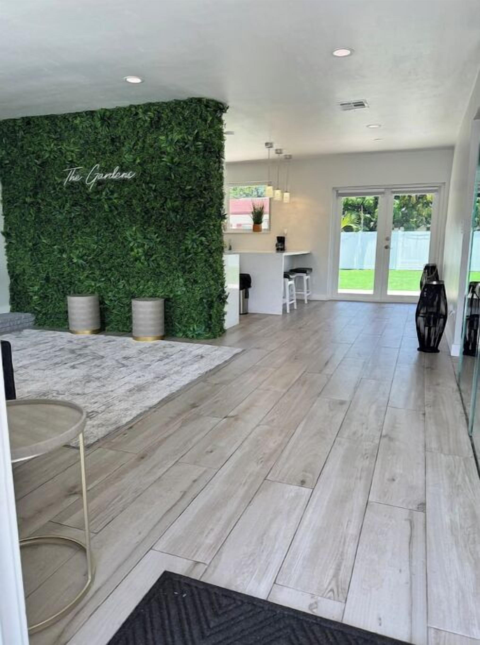 Ein geräumiger Raum mit Holzboden, einer grünen Wand mit dem Schriftzug 'The Garden', einer Küchenzeile und einer Glastür, die in einen Garten führt.