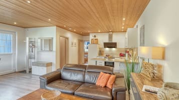 Ein modernes Wohnzimmer mit Ledersofa, einem Holztisch und einer Küche im Hintergrund.