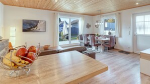 Eine moderne Küche mit Holzboden, ein Essbereich mit Tisch und Stühlen sowie ein Blick ins Freie durch große Fenster.