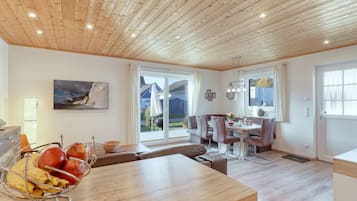Eine moderne Küche mit Holzboden, ein Essbereich mit Tisch und Stühlen sowie ein Blick ins Freie durch große Fenster.