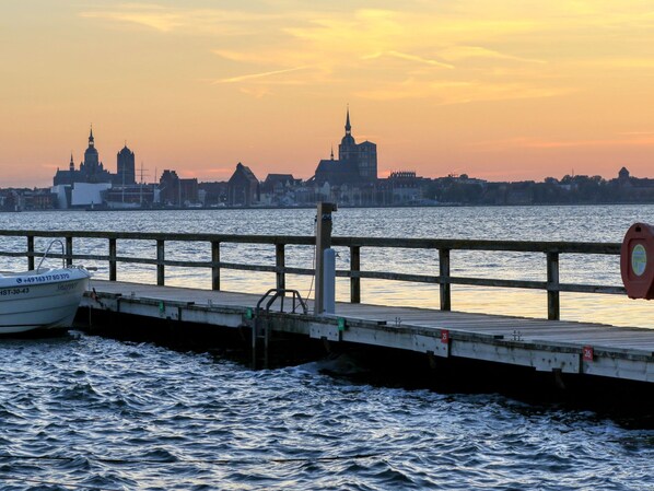 A waterfront view with a boat docked at a pier, a lifebuoy on the railing, and a city skyline in the background.