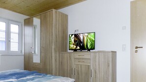 Un dormitorio con cama, armario, televisor sobre un mueble y una puerta.