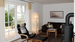 A living room with a black leather chair, a brown sofa, a wooden coffee table, and a black wood-burning stove. - Vacation home Katja by Interhome (Karlshagen)