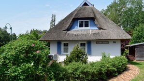 A traditional thatched-roof house with a white exterior and blue shutters, surrounded by lush greenery and a brick pathway. - Vacation home Katja by Interhome (Karlshagen)