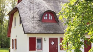 A house with a thatched roof, red shutters, and a stone foundation.