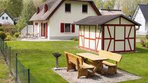 A traditional house with a thatched roof, a small attached shed, and a paved patio with wooden furniture.