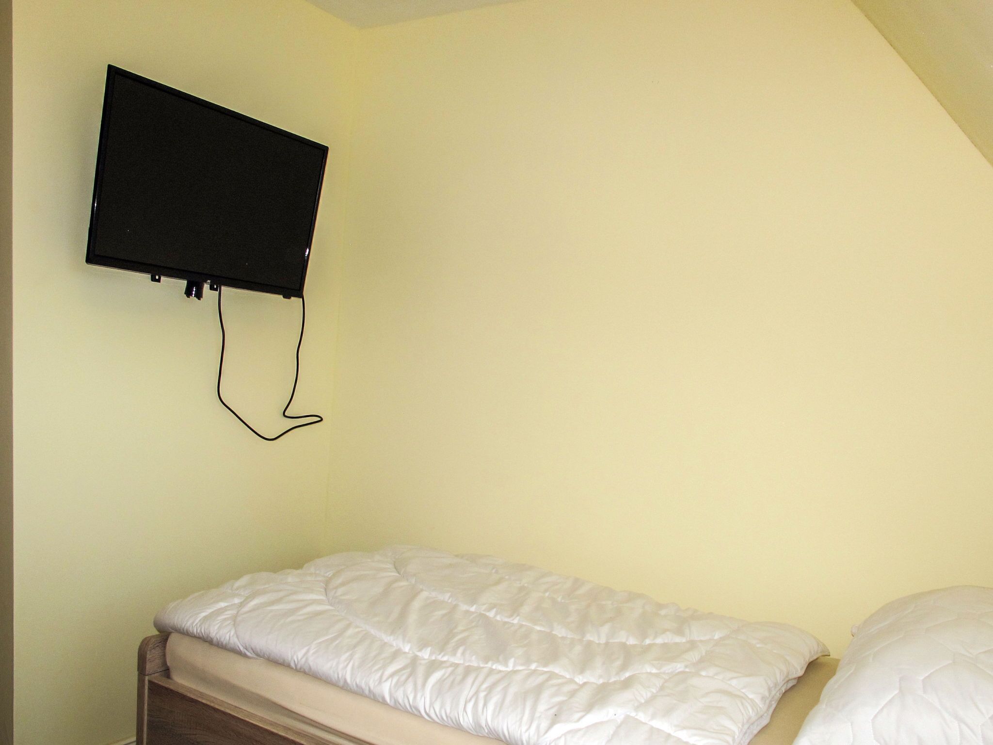 A single bed with a white duvet in a room with a light yellow wall and a mounted television.