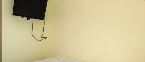 A single bed with a white duvet in a room with a light yellow wall and a mounted television.