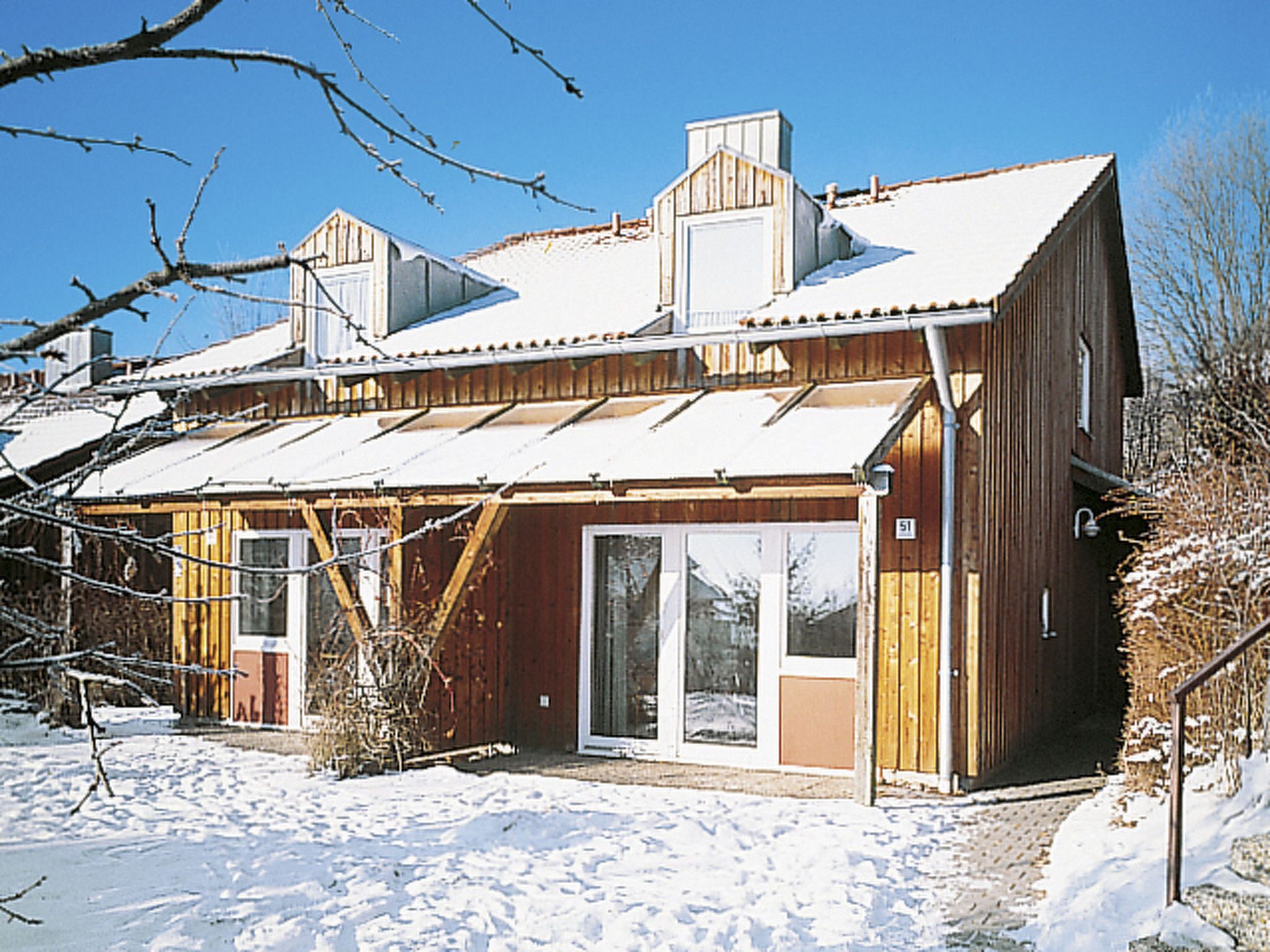 Een houten chalet met een metalen dak, grote schuifdeuren van glas en een bord met het nummer '51'.
