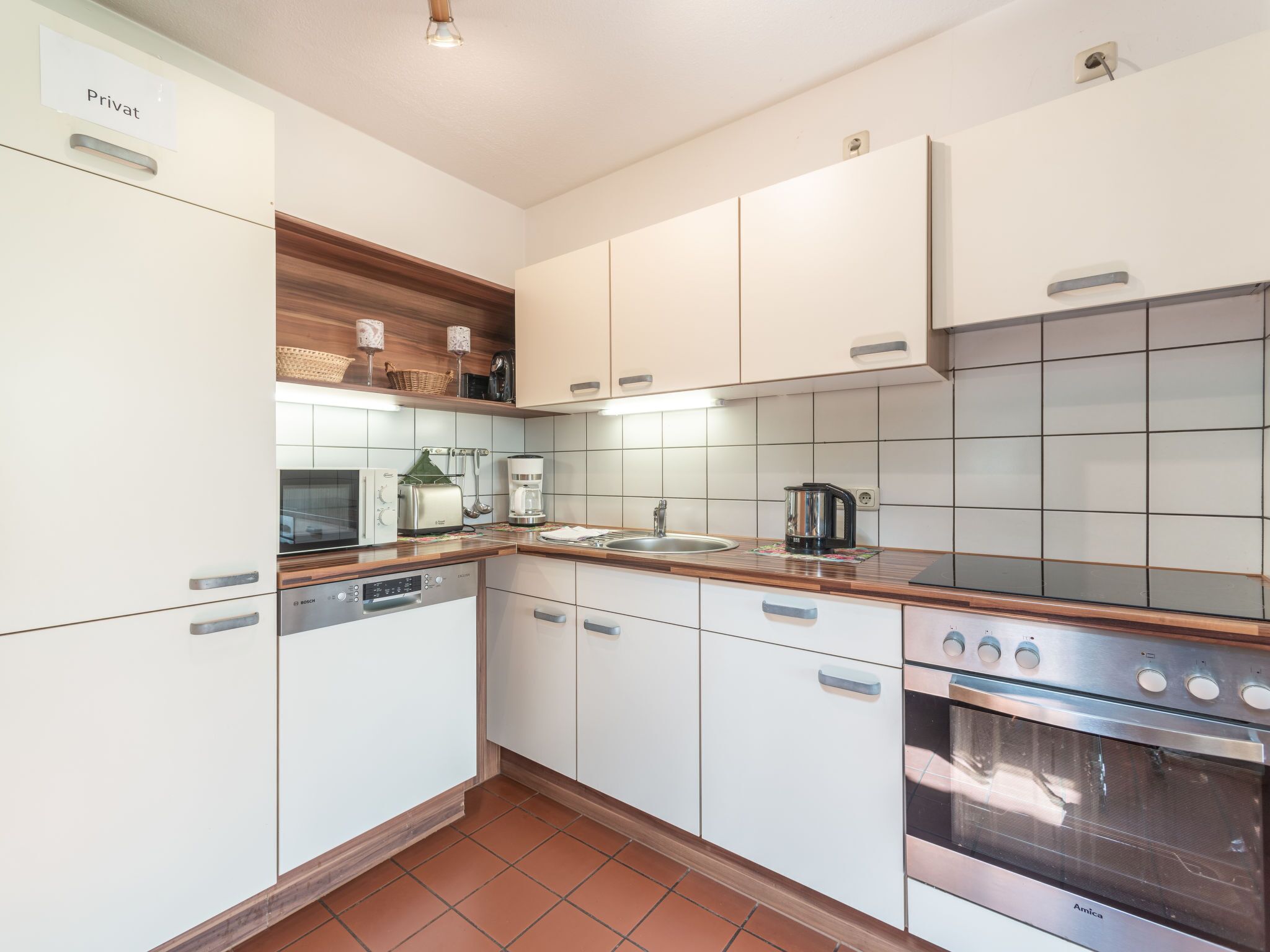 A modern kitchen with white cabinets, a Bosch dishwasher, a coffee maker, and an Amica oven.