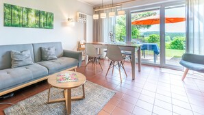 A modern living room with a sofa, coffee table, and dining area with chairs. There is a large window with an umbrella outside. - Schlossberg by Interhome (Zandt)