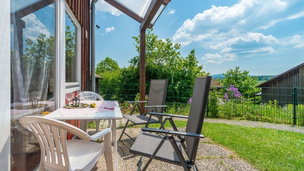 A patio with a table and chairs, a glass enclosure, and a view of a green landscape. - Ferienhäuser Schlossberg by Interhome (Zandt)