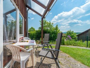 Eine Terrasse mit Tisch und Stühlen, einer Glaskonstruktion und Blick auf eine grüne Landschaft.
