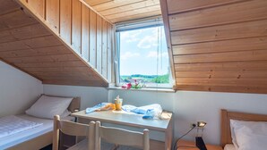 A small, cozy room with a sloped ceiling, a window with a view of greenery, a desk with a chair, and two single beds. - Ferienhäuser Schlossberg by Interhome (Zandt)