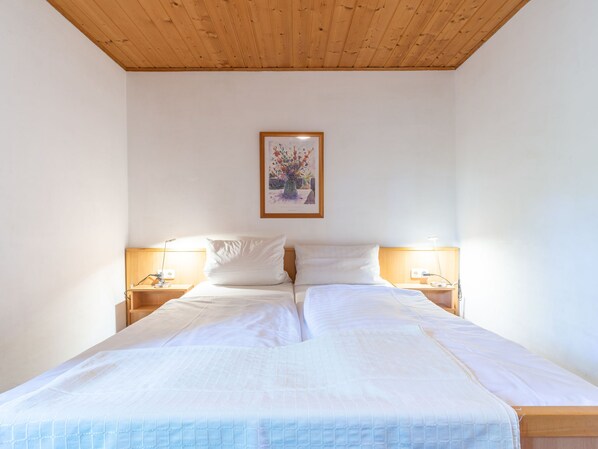Cama doble con ropa blanca, dos mesitas de noche con lámparas, y un cuadro con flores en la pared.