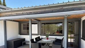 En overdækket terrasse med et bord, stole, en bænk og en potteplante.