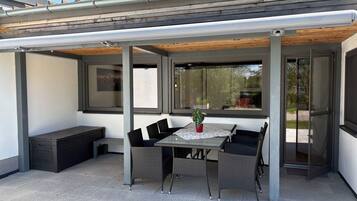 Ein überdachter Patio-Bereich mit Tisch, Stühlen, einer Bank und einem Topfpflanzen.