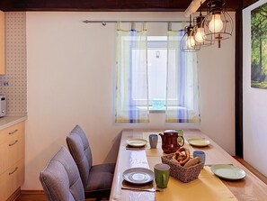 A dining area with a table set for two, a chair, a basket of pretzels, and a window with curtains.