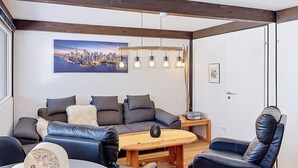 En moderne stue med en sofa, lænestole, et sofabord og et bybillede på væggen.
