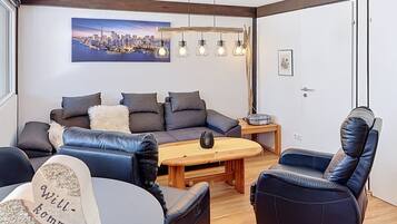 Ein modernes Wohnzimmer mit einer Couch, Sesseln, einem Couchtisch und einem Stadtbild an der Wand.