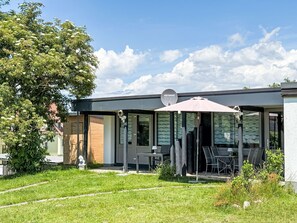 Un bâtiment moderne doté d’une antenne parabolique, d’un espace extérieur aménagé pour s’asseoir et d’une zone herbeuse.