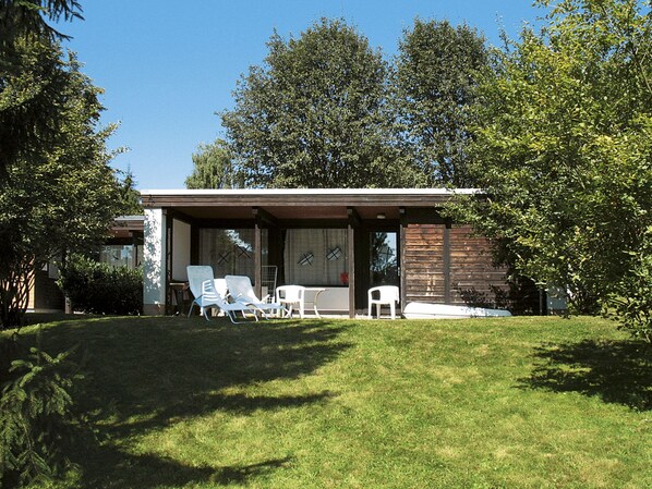 A modern house with a covered patio area, a lawn, and trees.