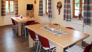 Un comedor con una mesa de madera, sillas rojas, cortinas a cuadros y un radiador.