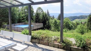 Un espacio al aire libre cubierto con piscina, mobiliario y vistas a un paisaje verde.