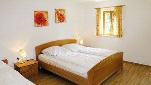 Un dormitorio con una cama de madera, mesitas de noche, una ventana con cortinas y dos cuadros en la pared.