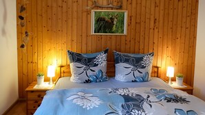 Ein Schlafzimmer mit Holzwand, zwei Nachttische mit Lampen, einem Bett mit floralem Bettbezug und einem Bild von einem Reh.