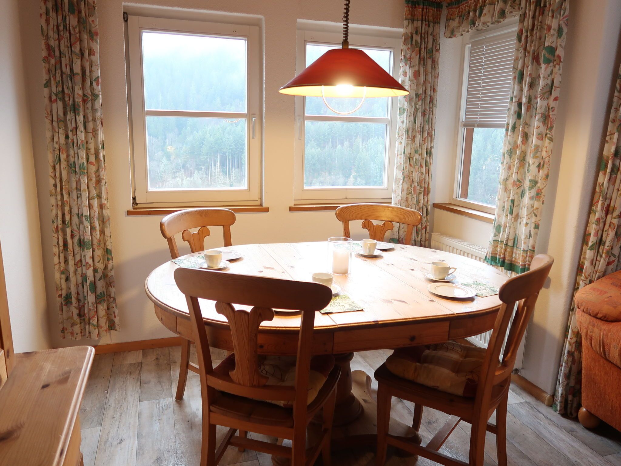Un coin repas avec une table ronde en bois, six chaises et une lampe rouge suspendue.