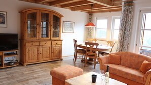 Een gezellige woonkamer met een houten kast, een televisie, een eettafel met stoelen en een bank.